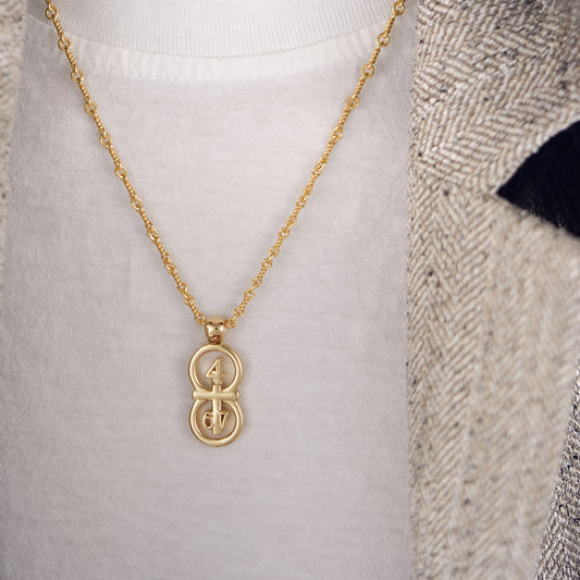 The  RIYAN 29 and 11® pendant has the numbers 4,6, and 7 intertwined with the cross to represent Philippians 4:6-7 with the chapter name "Phillipians" inscribed on the back.  Model is weaing a the large Riyan pendant in gold on an 18" Rolo chain.  Model is wearing a high neck T-shirt and a houndstooth blazer.