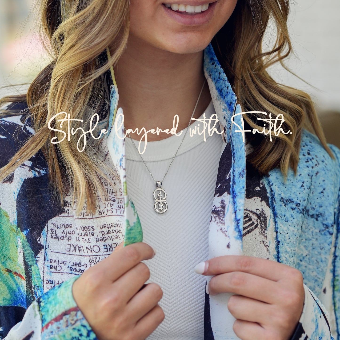 The silver RIYAN 29 and 11® pendant has the numbers 4 and 13 intertwined with the cross to represent Philippians 4:13 with the chapter word "Philippians" inscribed on the back. model is wearing the large silver Riyan pendant on an 18" Wheat chain. Model is wearing a white high neck tank and colorful blazer.