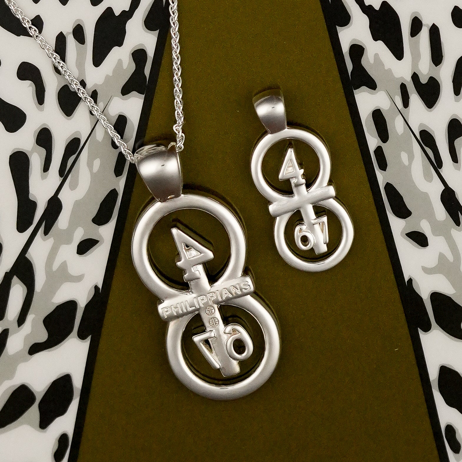 The silver RIYAN 29 and 11® pendant has the numbers 4,6, and 7 intertwined with the cross to represent Philippians 4:6-7 with the chapter name "Phillipians" inscribed on the back.