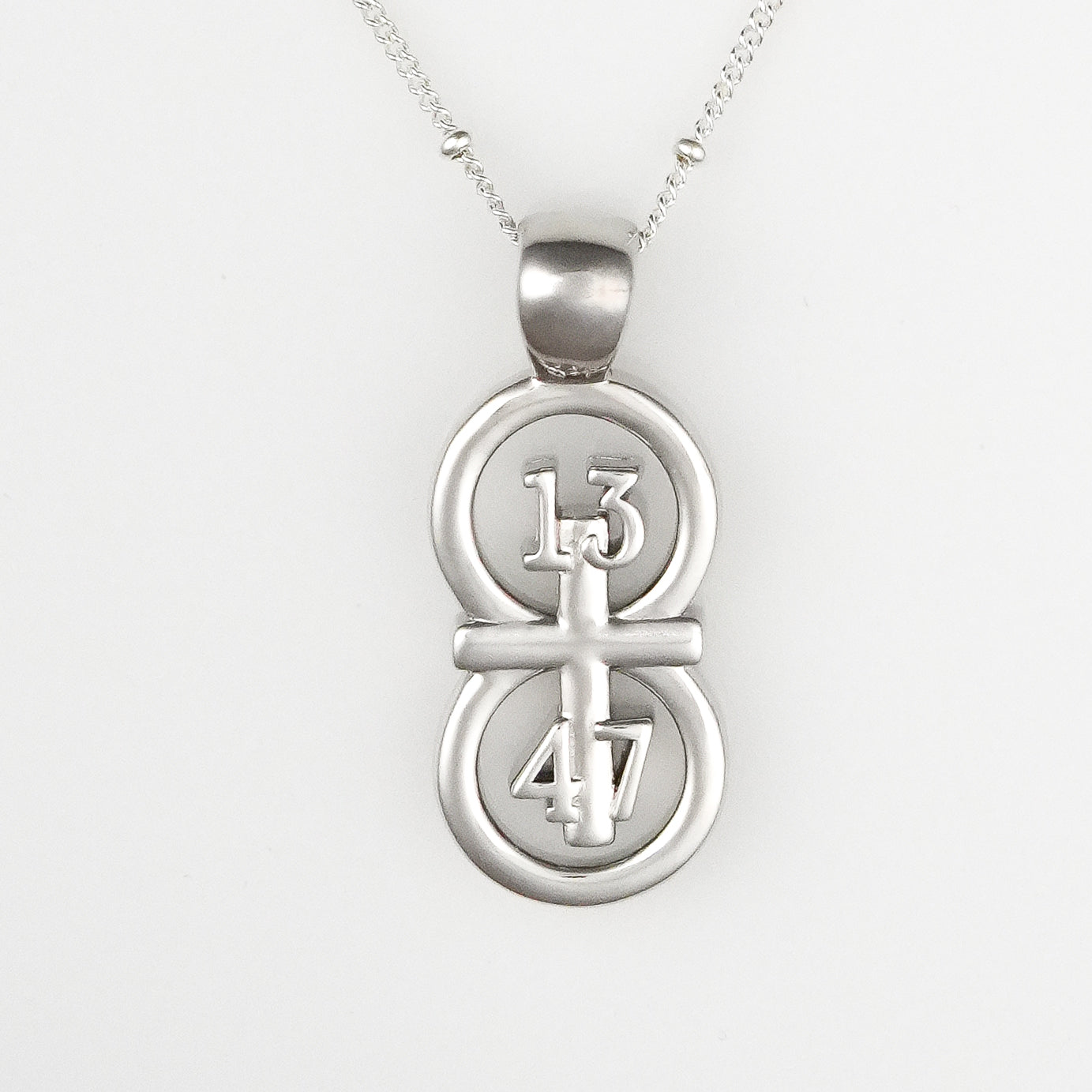The silver RIYAN 29 and 11® pendant has the numbers 13, 4, and 4 intertwined with the cross to represent 1 Corinthians 13:4-7 with the chapter word "1 Corinthians" inscribed on the back.