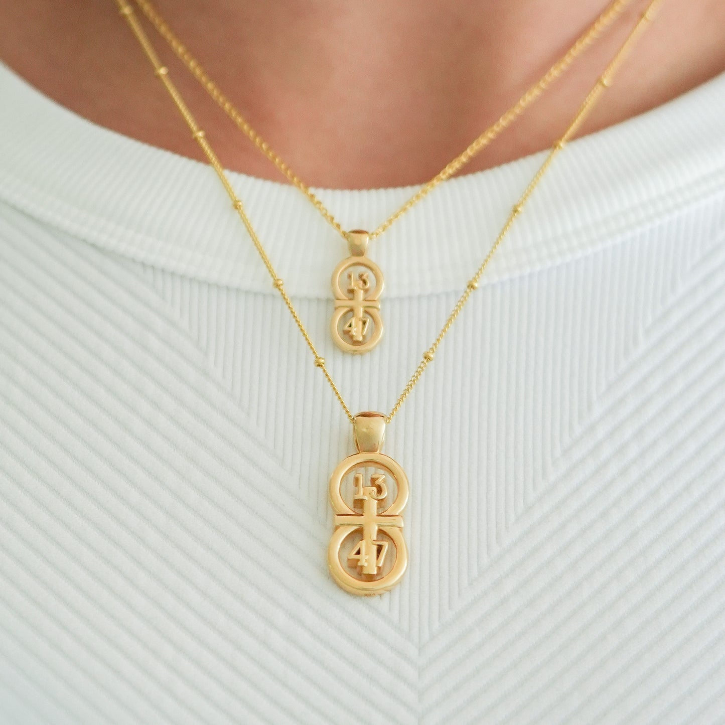 Gold small and large pendants displayed on neck with this wheat chain and satellite chain on the larger pendant.  The RIYAN 29 and 11® pendant has the numbers 13, 4, and 4 intertwined with the cross to represent 1 Corinthians 13:4-7 with the chapter word "1 Corinthians" inscribed on the back.