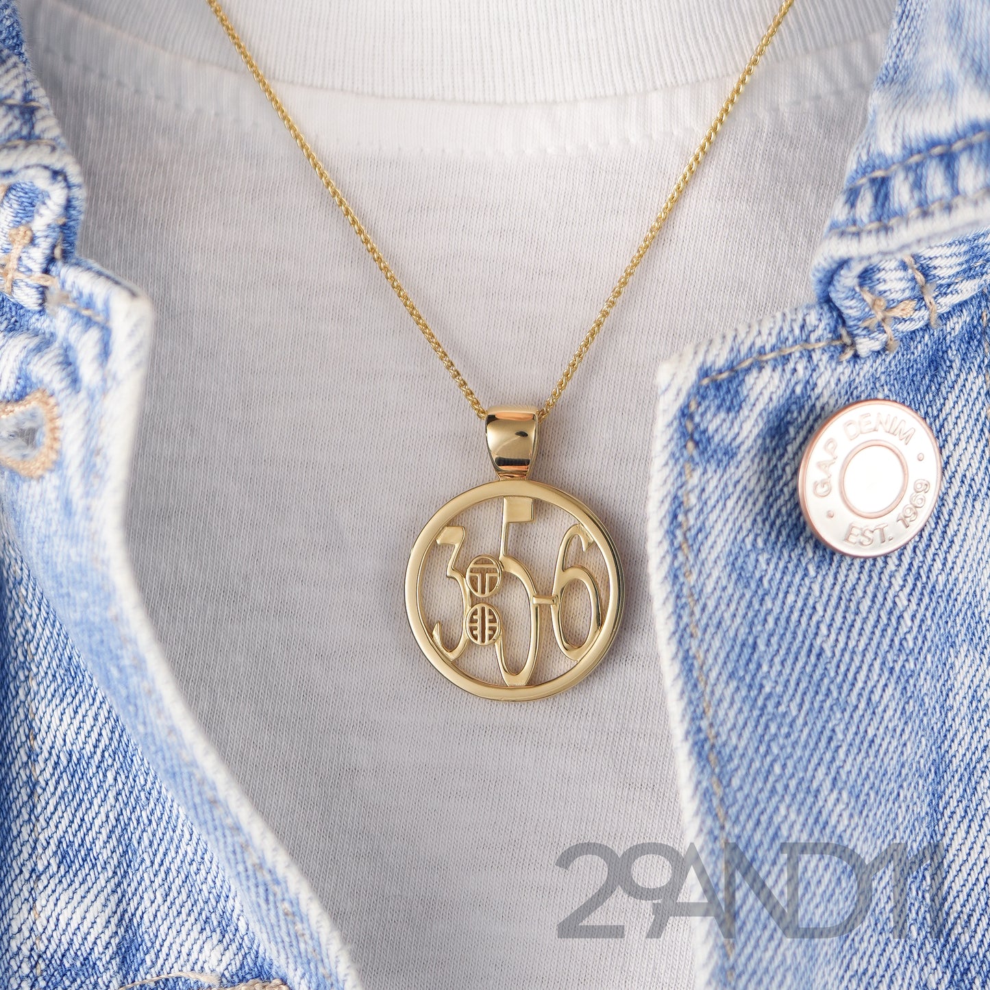 The Ashe is our monogram pendant inspired by our beloved monograms that grace all the thing we love and use daily. The numbers 3, 5, and 6 are stretched vertically to the edges of the pendant. The numbers 3, 5, and 6 are separated by a colon which is represented by our logo.Down the vertical side of the pendant the chapter name Proverbs is inscribed on the monogram pendant.  Model is wearing the pendant on a 18" wheat chain against a white high neck tank and denim jacket.