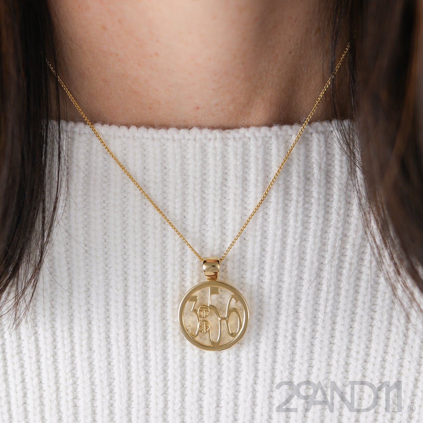 The Ashe is our monogram pendant inspired by our beloved monograms that grace all the thing we love and use daily. The numbers 3, 5, and 6 are stretched vertically to the edges of the pendant. The numbers 3, 5, and 6 are separated by a colon which is represented by our logo.Down the vertical side of the pendant the chapter name Proverbs is inscribed on the monogram pendant.  Model is wearing the pendant on a 18" wheat chain and a white ribbed sweater.