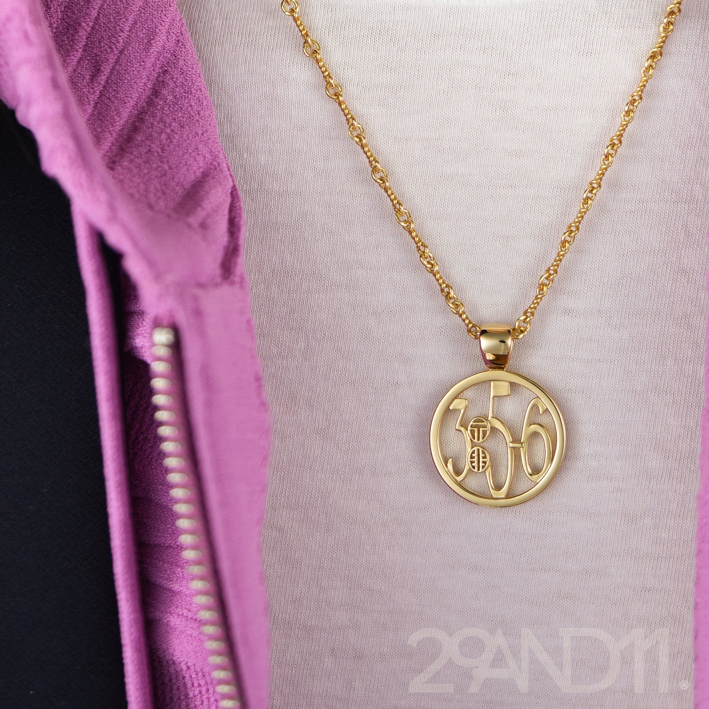 The Ashe is our monogram pendant inspired by our beloved monograms that grace all the thing we love and use daily. The numbers 3, 5, and 6 are stretched vertically to the edges of the pendant. The numbers 3, 5, and 6 are separated by a colon which is represented by our logo.Down the vertical side of the pendant the chapter name Proverbs is inscribed on the monogram pendant.  Model is wearing the pendant on a 18" rolo chain against a white t-shirt and pink Veronica beard sweater.