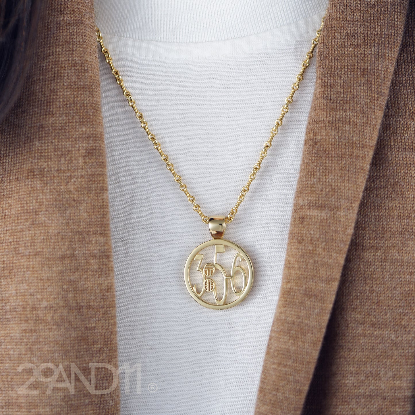 The Ashe is our monogram pendant inspired by our beloved monograms that grace all the thing we love and use daily. The numbers 3, 5, and 6 are stretched vertically to the edges of the pendant. The numbers 3, 5, and 6 are separated by a colon which is represented by our logo.Down the vertical side of the pendant the chapter name Proverbs is inscribed on the monogram pendant.  Model is wearing the pendant on a 18" Rolo chain against a high neck white t-shirt and brown scarf.