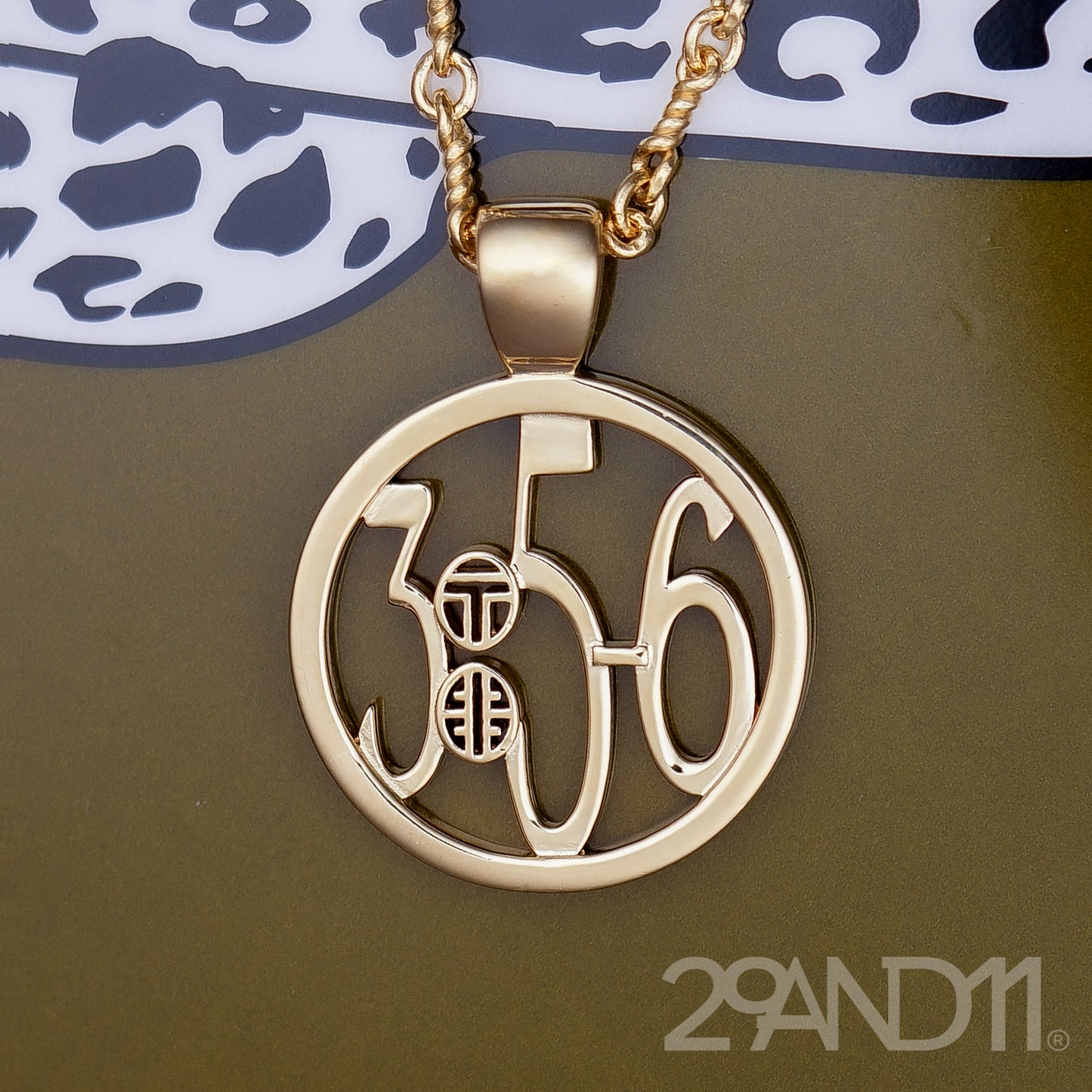 The Ashe is our monogram pendant inspired by our beloved monograms that grace all the thing we love and use daily. The numbers 3, 5, and 6 are stretched vertically to the edges of the pendant. The numbers 3, 5, and 6 are separated by a colon which is represented by our logo.Down the vertical side of the pendant the chapter name Proverbs is inscribed on the monogram pendant.  Model is wearing the pendant on a 18" Rolo chain against a Jonathan Adler leopard box.