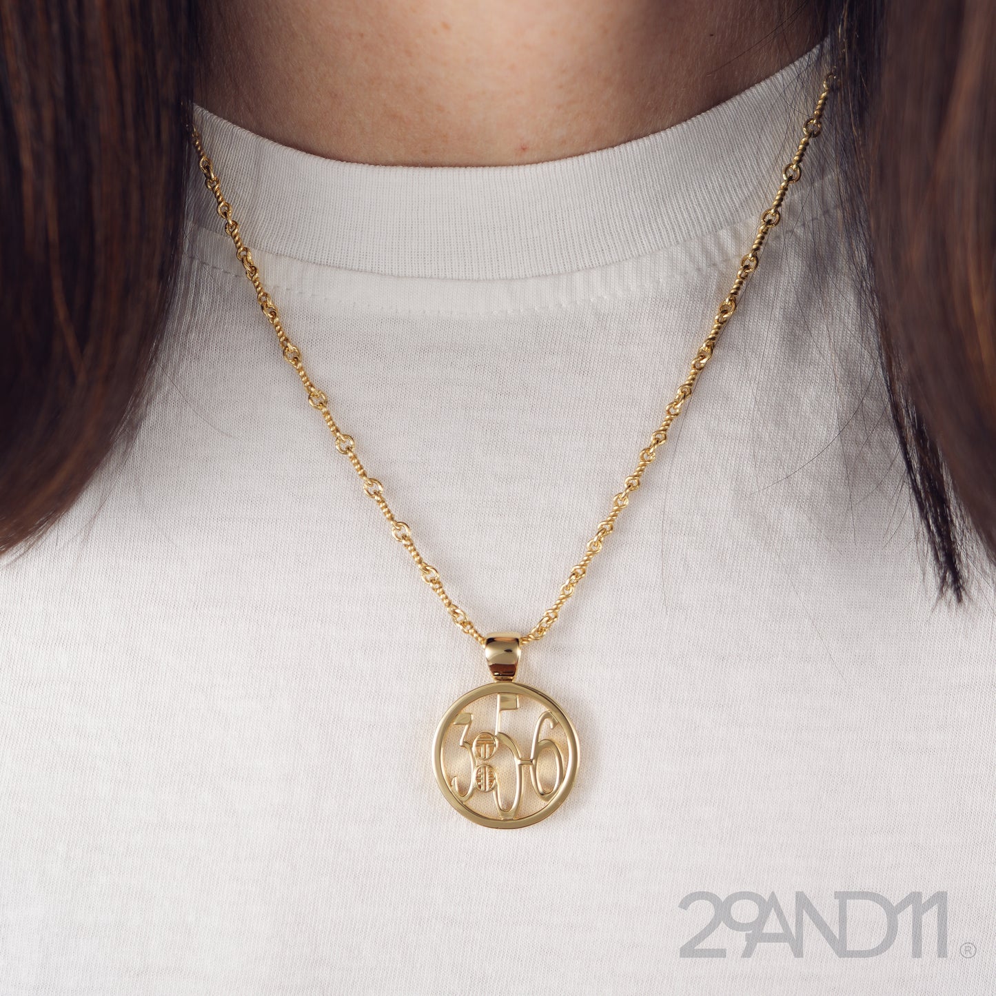 The Ashe is our monogram pendant inspired by our beloved monograms that grace all the thing we love and use daily. The numbers 3, 5, and 6 are stretched vertically to the edges of the pendant. The numbers 3, 5, and 6 are separated by a colon which is represented by our logo.Down the vertical side of the pendant the chapter name Proverbs is inscribed on the monogram pendant.  Model is wearing the pendant on a 18" wheat chain on a white high neck t-shirt.