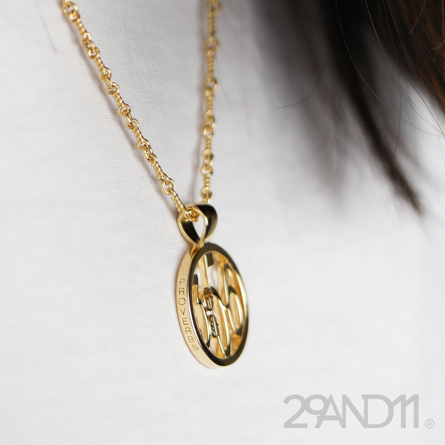 The Ashe is our monogram pendant inspired by our beloved monograms that grace all the thing we love and use daily. The numbers 3, 5, and 6 are stretched vertically to the edges of the pendant. The numbers 3, 5, and 6 are separated by a colon which is represented by our logo.Down the vertical side of the pendant the chapter name Proverbs is inscribed on the monogram pendant.  Model is wearing the pendant on a 18" rolo chain and the side engraving of the name is shown.