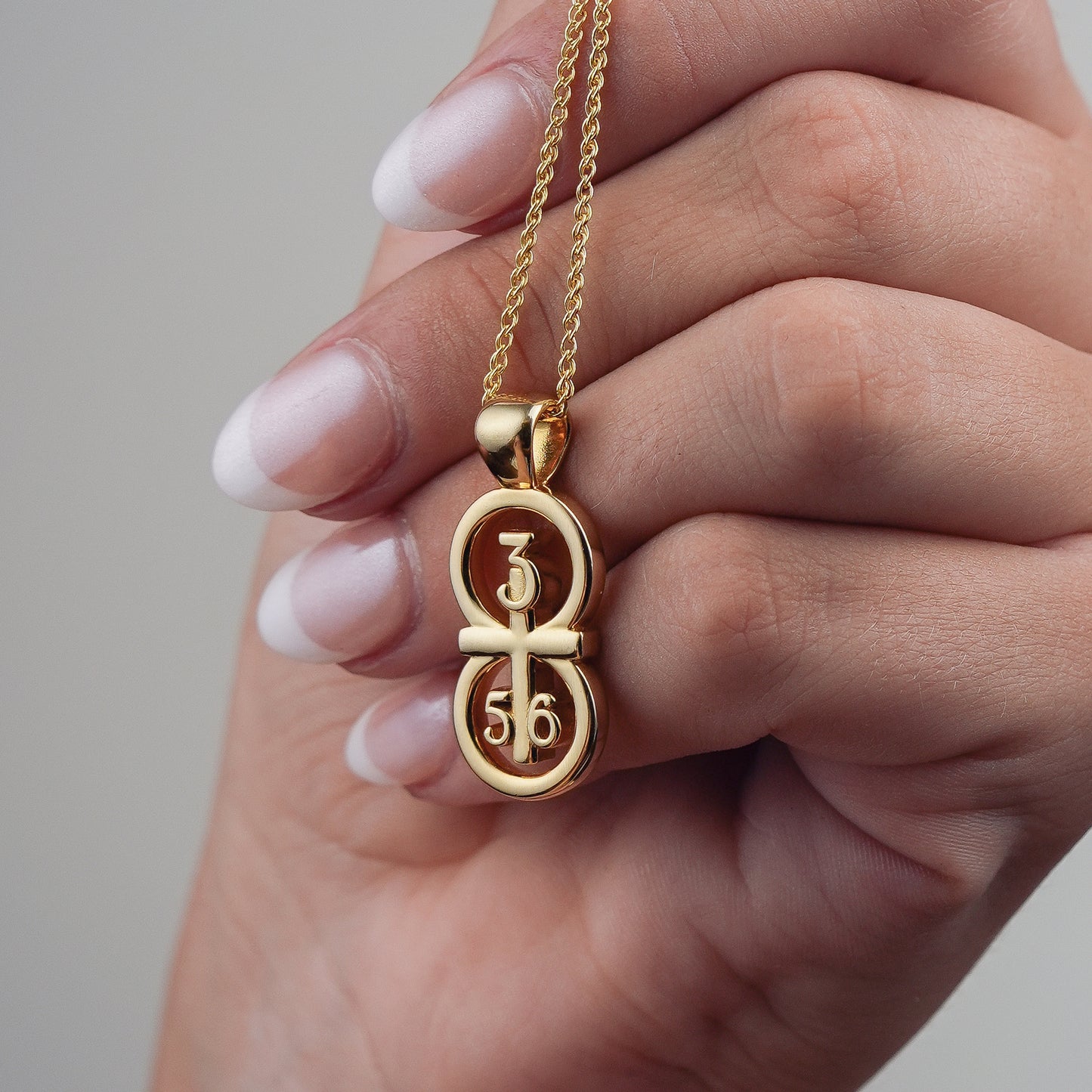 This picture displays our large pendant on our 14k gold filled wheat chain.  The pendant is draped over a hand for size comparison. Our RIYAN 29 and 11® pendant has the numbers 3, 5, and 6 intertwined with the cross to represent Proverbs 3:5-6 with the chapter word "Proverbs" inscribed on the back.