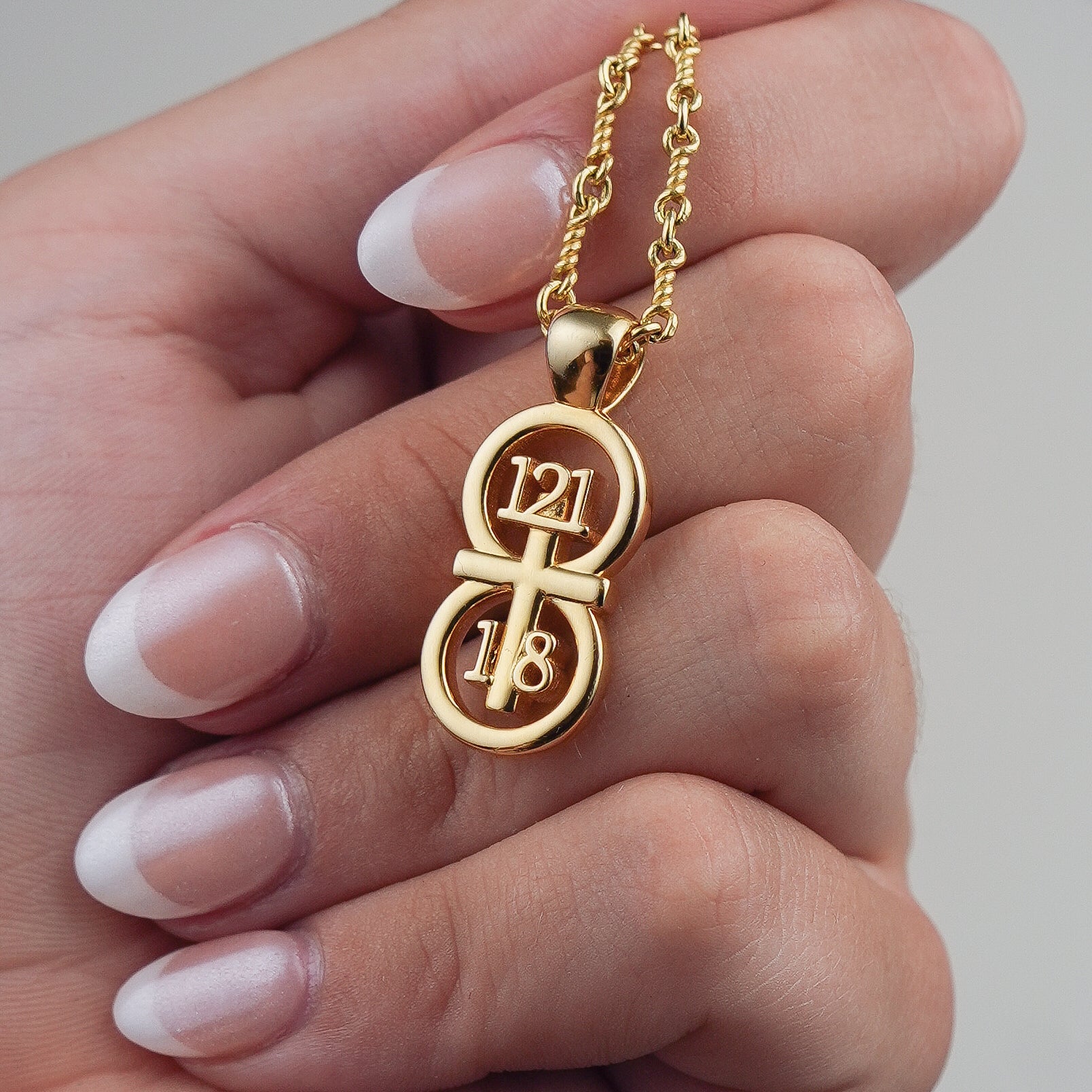 Our large pendant displayed draped over a hand with our 14k gold filled Rolo chain.  The RIYAN 29 and 11® pendant has the numbers 121, 1, and 8 intertwined with the cross to represent Psalm 121:1-8 with the chapter word "Psalm" inscribed on the back.