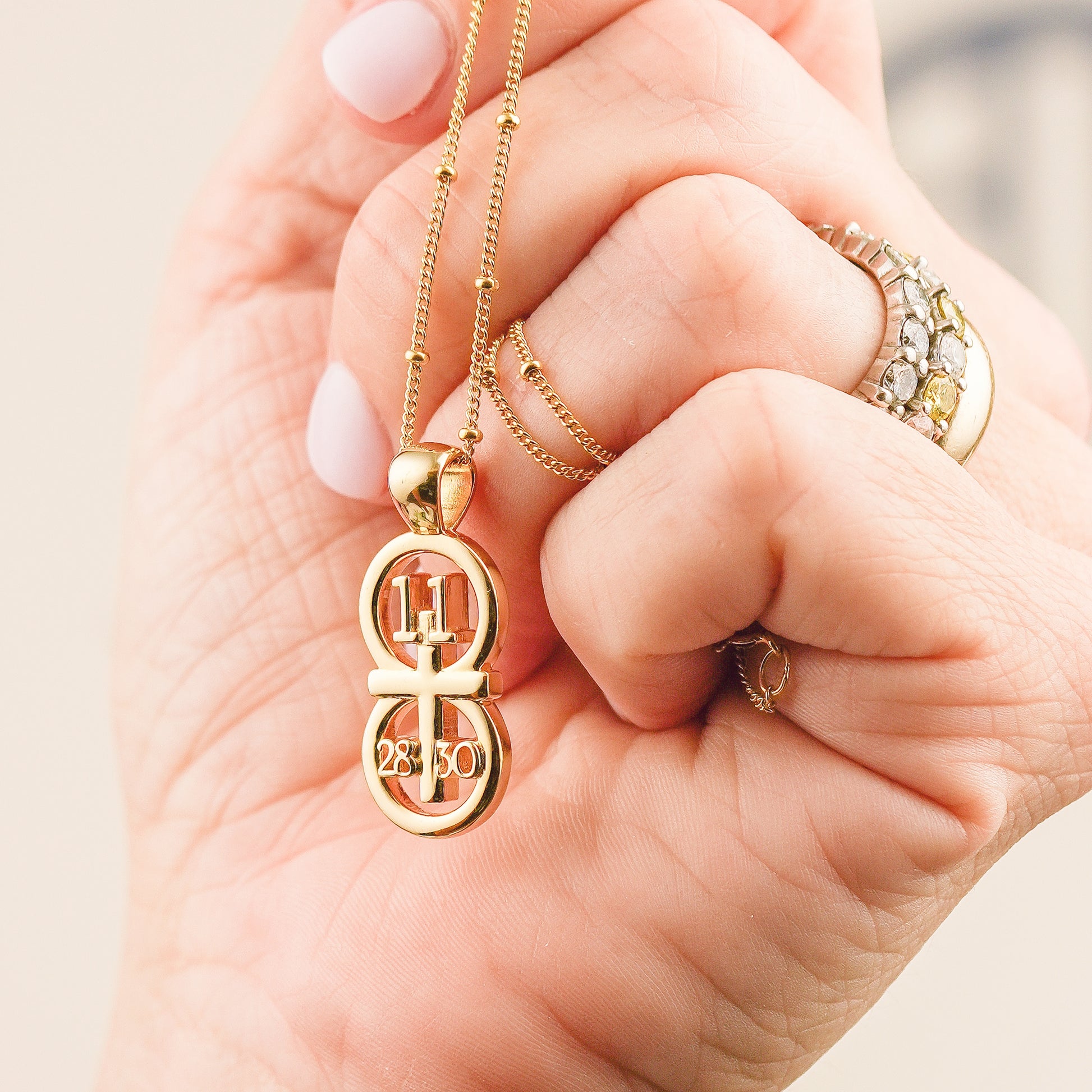 This picture displays our large pendant on our 14k gold filled satellite chain.  The pendant is draped over a hand for size comparison.  The RIYAN 29 and 11® pendant has the numbers 11, 28, and 30 intertwined with the cross to represent Matthew 11:28-30 with the chapter word "Matthew" inscribed on the back.