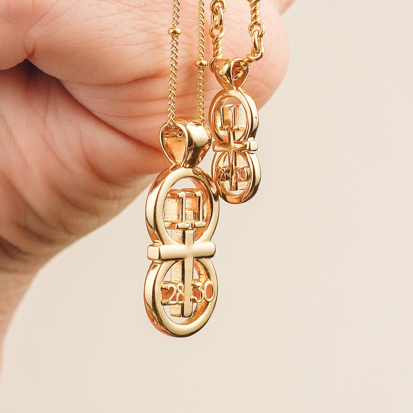 This picture displays our large pendant on our 14k gold filled satellite chain and small pendant on our 14k golf filled Rolo chain. The pendant is draped over a hand for size comparison. The RIYAN 29 and 11® pendant has the numbers 11, 28, and 30 intertwined with the cross to represent Matthew 11:28-30 with the chapter word "Matthew" inscribed on the back.
