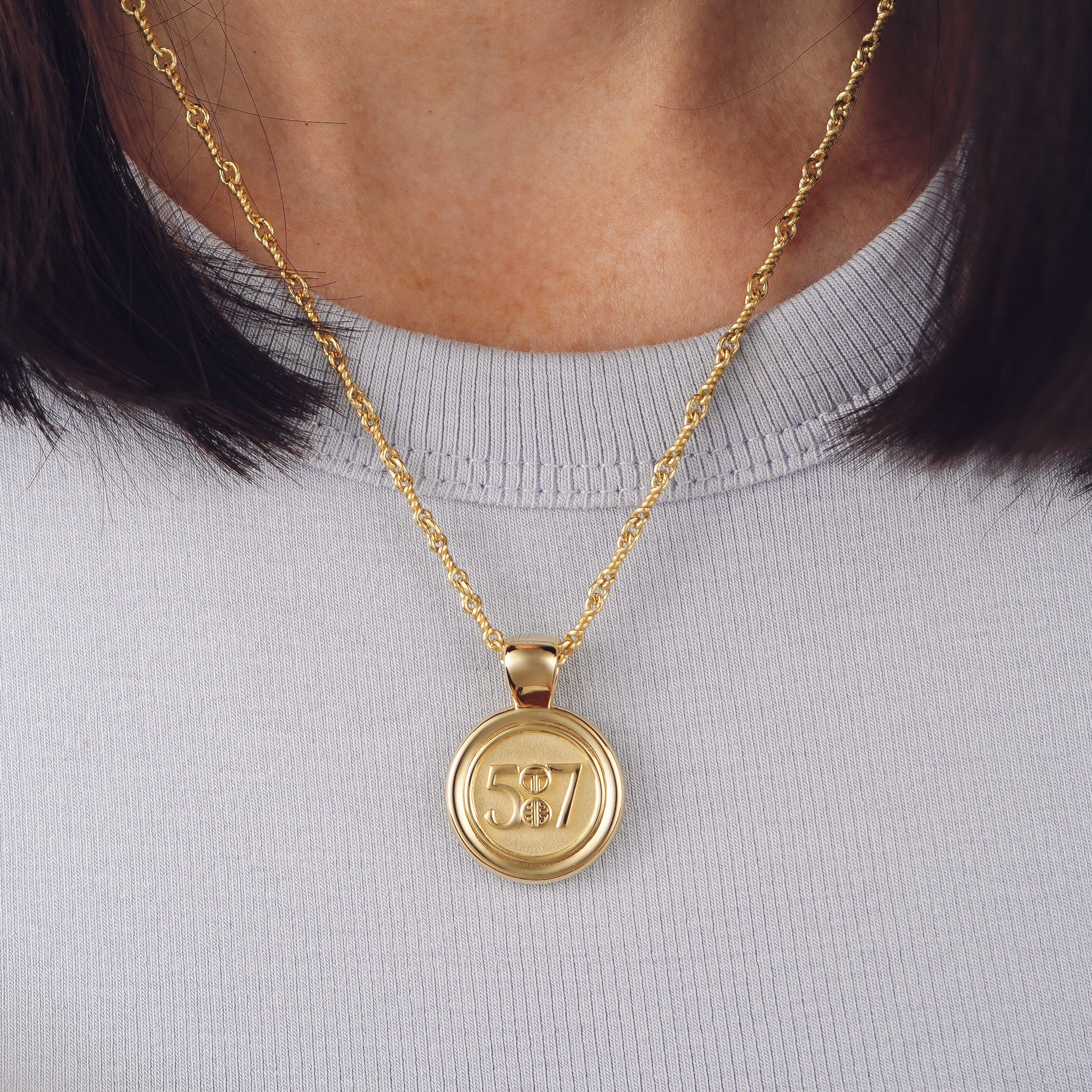 The WYIT is our first reversible pendant.&nbsp; One side of the medallion has the numbers 5 and 7 with our logo displayed as the colon between the chapter and verse.&nbsp; &nbsp;The other side of the pendant has a raised two tier cross. Down the vertical side of the pendant the chapter name 2 Corinthians is inscribed on the medallion.  Model is wearing the pendant on our 18" Rolo chain Model is wearing a light blue high neck tank.