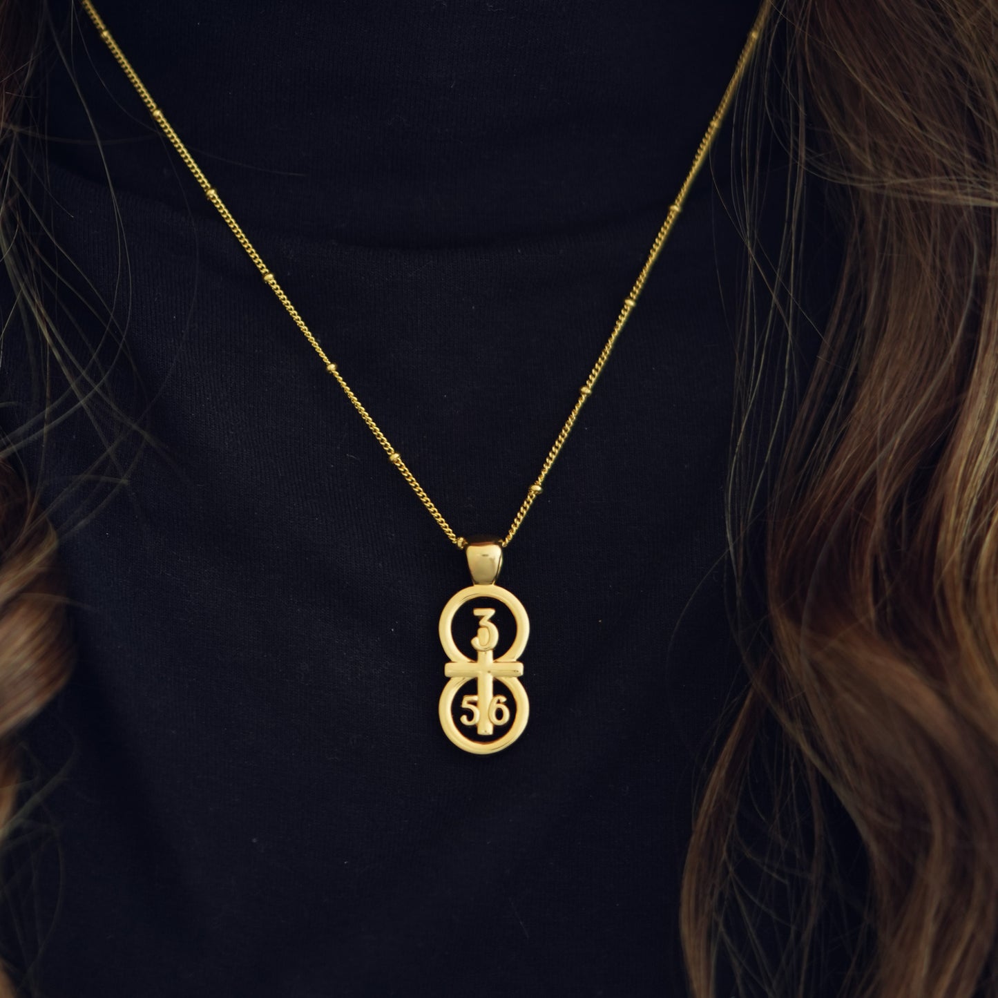 Gold large pendants displayed on the neck against a black shirt with our 14k gold filled satellite chain. Our RIYAN  29 and 11® pendant has the numbers 3, 5, and 6 intertwined with the cross to represent Proverbs 3:5-6 with the chapter word "Proverbs" inscribed on the back.